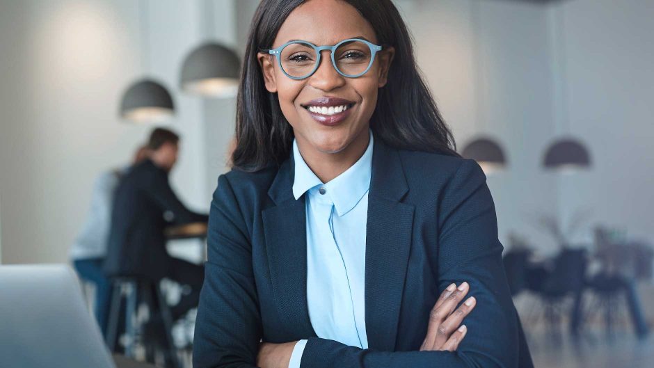 An African American woman in a blue blazer with trendy eyeglasses smiles at the camera