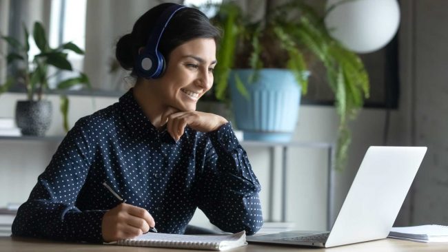 A university student wearing headphones smiles at her laptop